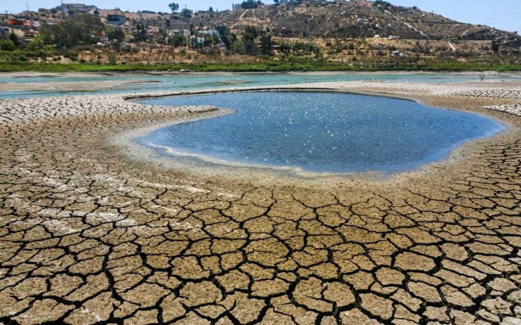 Um lago quase seco com o solo rachado ao redor, destacando os impactos das mudanças climáticas na disponibilidade de água.