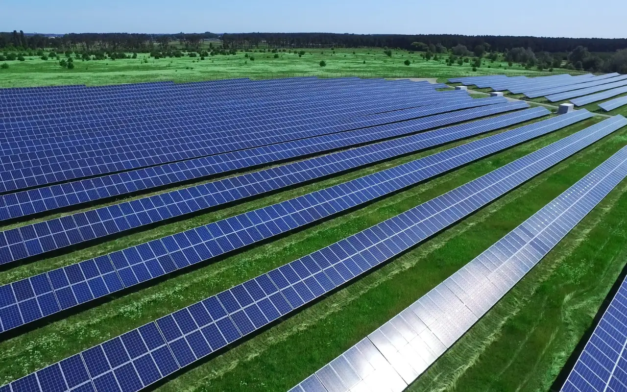Um grande campo de painéis solares instalados sobre um gramado verde, representando a produção de energias limpas a partir de fontes renováveis como o sol.